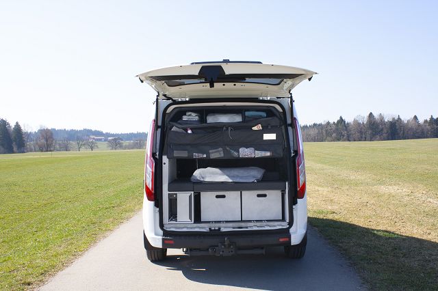 Weißer Globevan mit offener Kofferraumklappe und fertig gepackt mit Kofferraumtasche und zwei Kisten