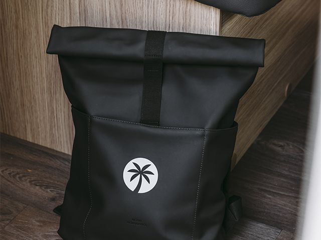 Schwarzer Rucksack mit weißem Sunligt Logo steht auf Holzboden